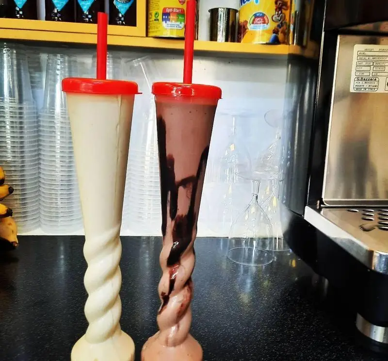 شیک‌های خنک و خوش طعم وانیلی و شکلاتی در لیوان‌های بلند پیچ‌دار با در و نی قرمز در آبمیوه بستنی ویتامینه آریا.