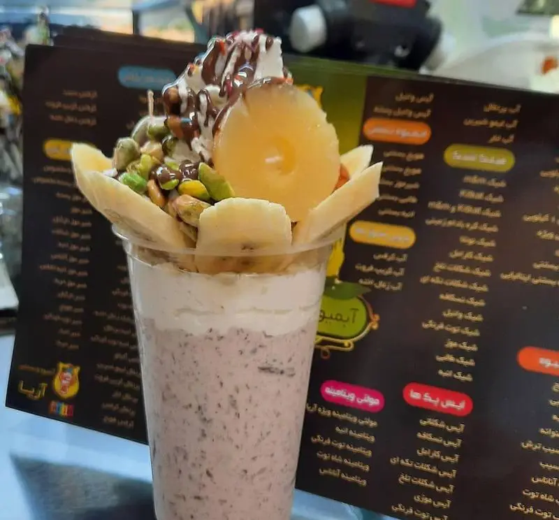 نوشیدنی شیک توت فرنگی لایه‌ای با خامه، موز، آناناس و پسته تزئین شده، محصولی جذاب از آبمیوه بستنی ویتامینه آریا.