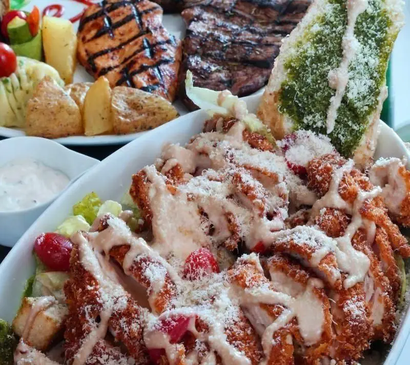 نمایی نزدیک از سالاد سزار ویژه رستوران فرنگی ویکند با مرغ سوخاری، سس مخصوص و پنیر، در کنار استیک و جوجه گریل.