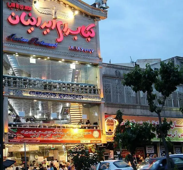 نمای بیرونی و شبانه رستوران و کبابسرای ایرانیان در تهران، با تابلوی بزرگ و نورانی، ارائه کننده انواع کباب، آش، حلیم و غذاهای سنتی و اصیل ایرانی.