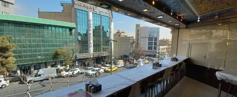 رستوران ایرانیان: چشم انداز دلنشین شهری از داخل رستوران با میزهای آماده و فضایی آرام برای صرف غذا و لذت بردن از محیط.