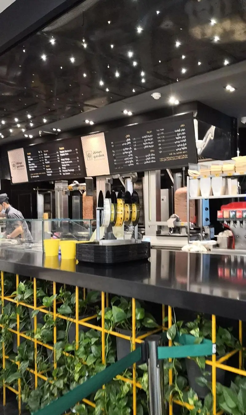 تصویری از فضای داخلی مدرن رستوران دونر گاردن، شامل پیشخوان مشکی، منوهای دیجیتال و دونر کباب. دیوار سبز و نورپردازی جذاب.