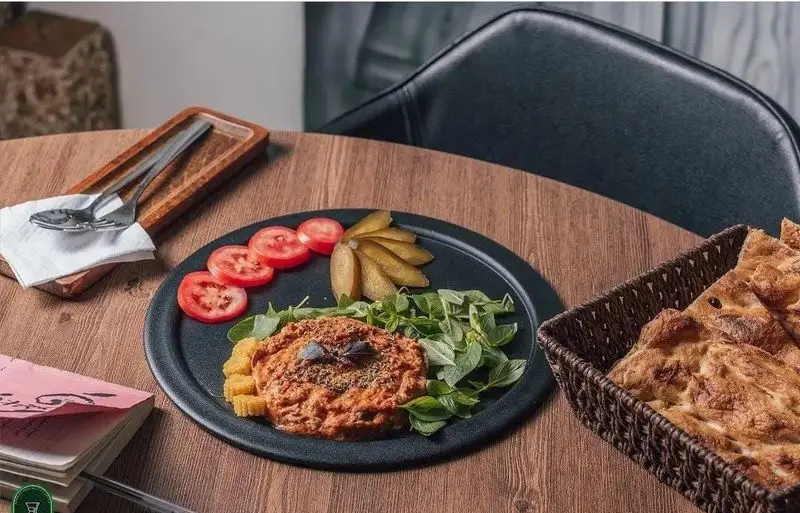 غذای سنتی و خوشمزه در کافه رستوران آژمان شامل دیپ یا خورش گوجه با سبزیجات معطر، نان تازه و دورچین گوجه و ترشی.