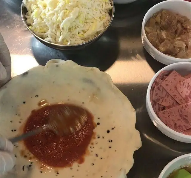 تهیه پیتزای لذیذ در فست فود برگر هال: پخش سس روی خمیر، افزودن پنیر و ترکیبات گوشتی تازه برای طعم بی‌نظیر.