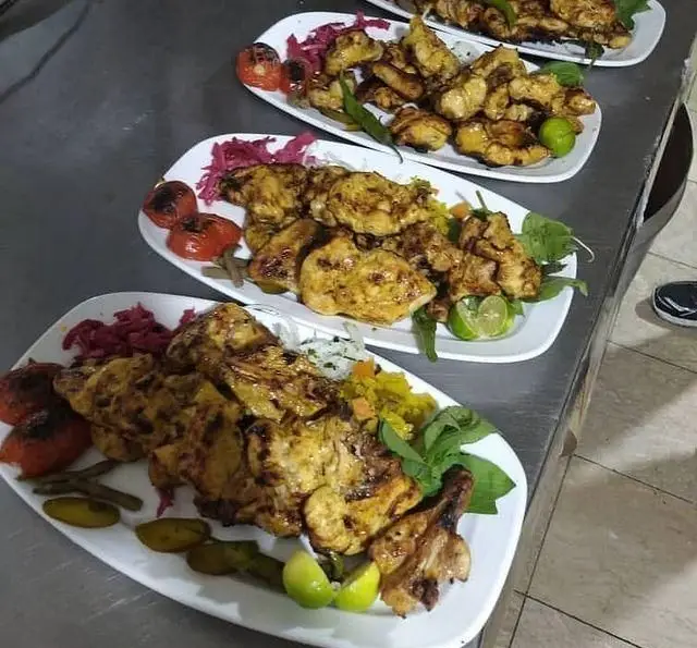 چندین بشقاب جوجه کباب زعفرانی و لذیذ با گوجه کبابی، ترشی، لیمو تازه و سبزیجات معطر در باغچه رستوران دیپلمات.