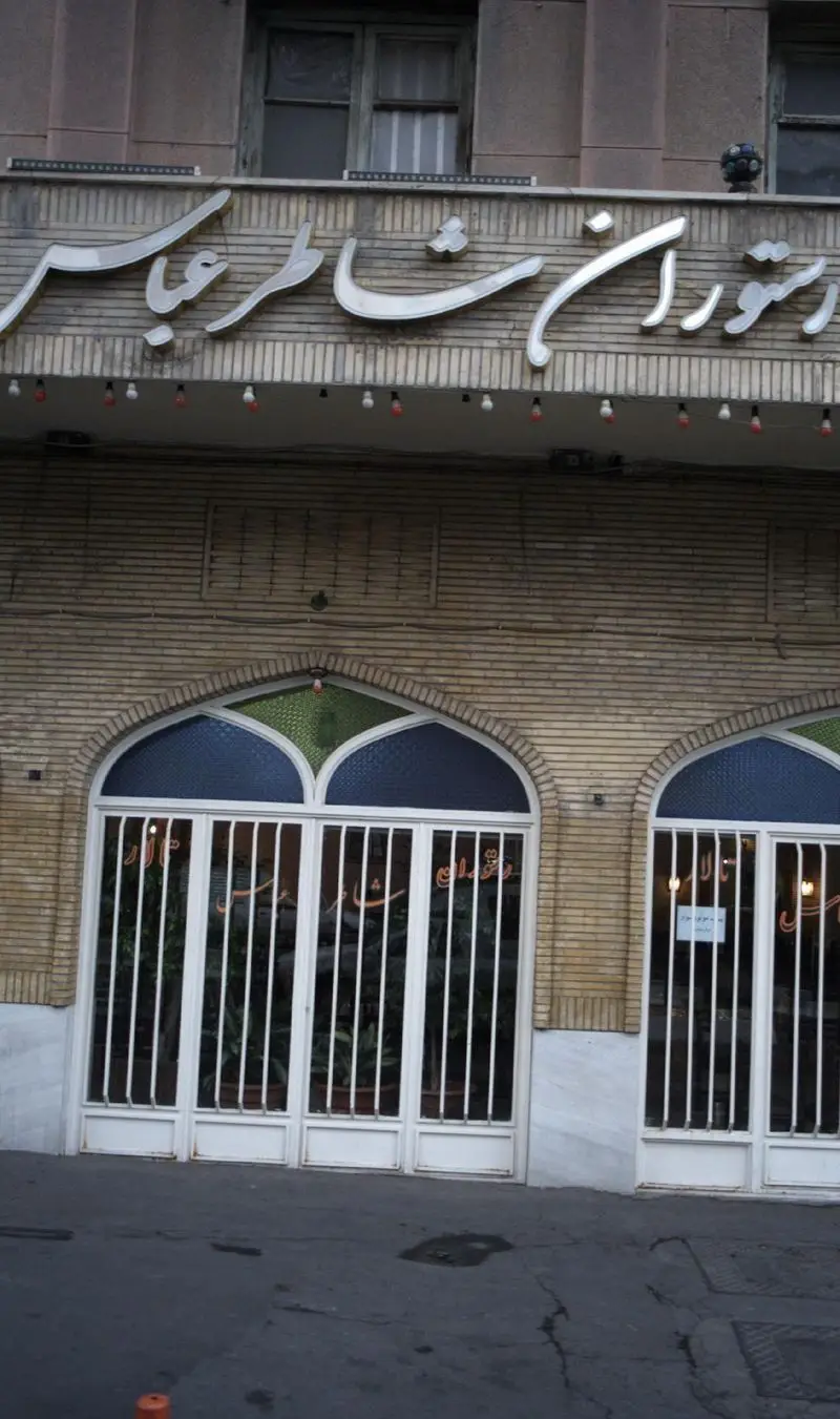 تصویری از نمای بیرونی رستوران شاطر عباس، شامل تابلوی درخشان فارسی، سردر آجری با طاق‌های زیبا و درب‌های ورودی کلاسیک و سنتی.