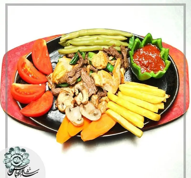 بشقاب سیزلر رستوران شاطر عباس شامل تکه‌های فیله مرغ و گوشت، قارچ، سیب‌زمینی سرخ‌کرده، لوبیا سبز، هویج و گوجه فرنگی با سس.