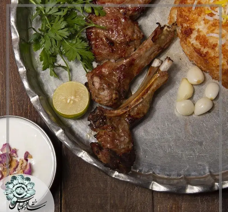 تصویری جذاب از کباب شیشلیک بره لذیذ رستوران شاطر عباس همراه با ته دیگ زعفرانی، لیمو، جعفری و سیر تازه؛ غذای سنتی ایرانی.