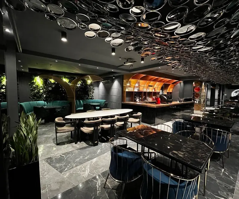 دکوراسیون داخلی مدرن کافه رستوران هوکاجی با سقف آینه‌ای خاص، مبلمان لوکس سبز و میزهای مرمری مشکی، فضایی دلنشین و شیک.
