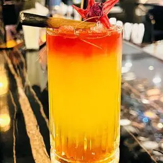 نوشیدنی کوکتل رنگین کمانی زیبا و خوشمزه در کافه رستوران هوکاجی، با لایه‌های زرد و قرمز، تزئین شده با گل و چوب دارچین برای لذت تابستانی.