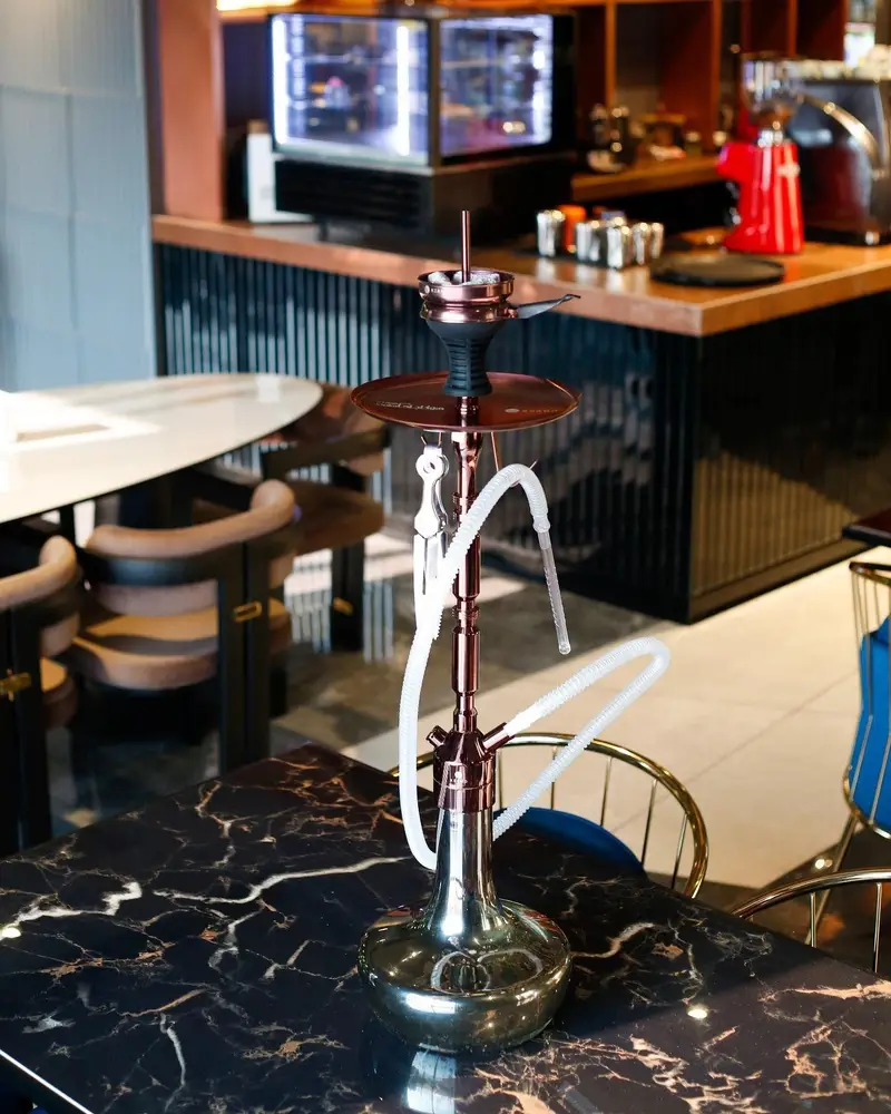 قلیان لوکس و مدرن در فضای داخلی کافه رستوران هوکاجی، روی میز مرمری مشکی با رگه‌های طلایی و بار شیک.