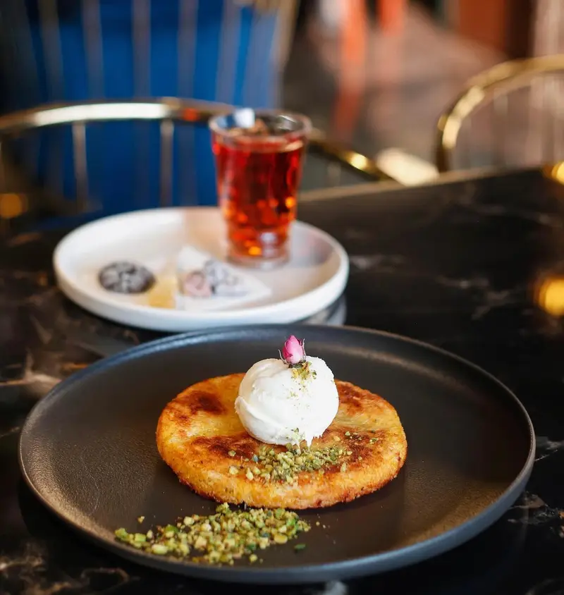 دسر لذیذ کونفه با بستنی، پسته و غنچه گل رز در کافه رستوران هوکاجی. چای گرم در پس‌زمینه تکمیل‌کننده این تجربه دلنشین است.