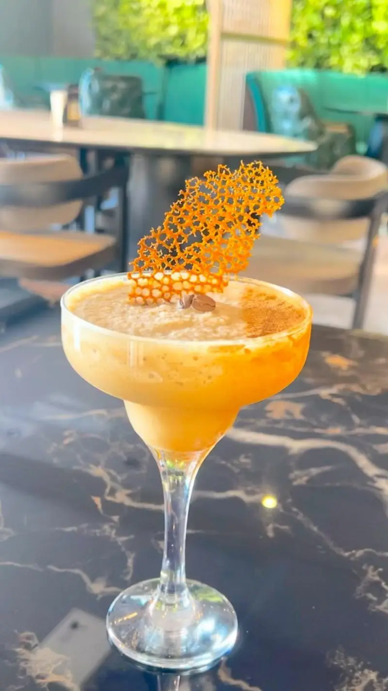 نوشیدنی خوشمزه قهوه در لیوان مارگاریتا با تزیین کاراملی و دانه قهوه در کافه رستوران هوکاجی، فضایی دلنشین برای استراحت.