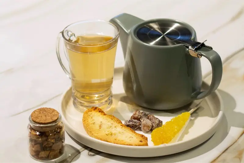 سرو چای یا دمنوش با قوری و فنجان شیشه‌ای، همراه با نبات زرد، کوکی و تنقلات دیگر در کافه رستوران هوکاچی.