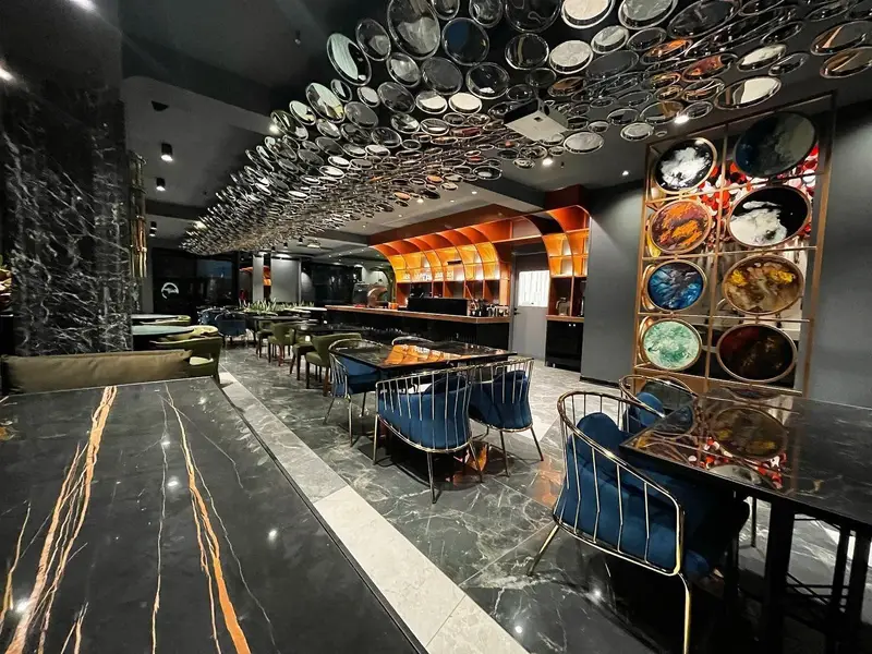 فضای داخلی لوکس و مدرن کافه رستوران هوکاجی با میزهای مرمری مشکی، صندلی‌های مخمل آبی و دکوراسیون سقف شیک و هنری.