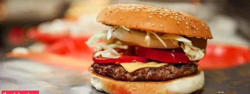 همبرگر خوشمزه و تازه فست فود چیتر چیکن با نان کنجدی، گوشت گریل، پنیر، کاهو و گوجه فرنگی آماده سرو در بهترین فست فود شهر.