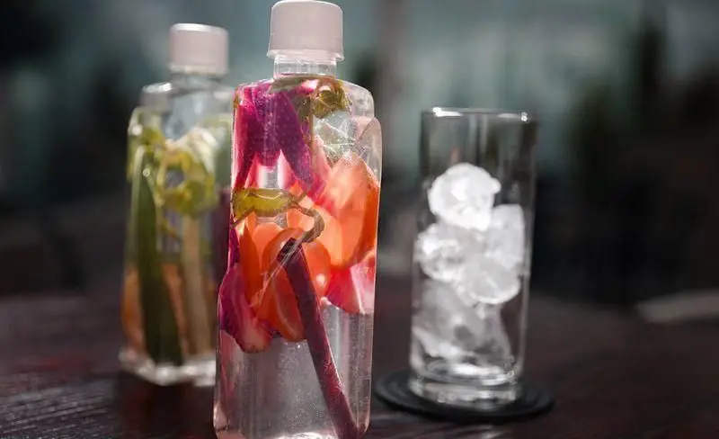 نوشیدنی‌های میوه‌ای تازه و گوارا در بطری‌های شیک، همراه با لیوانی پر از یخ آماده برای سرو در فست فود چیتر چیکن.