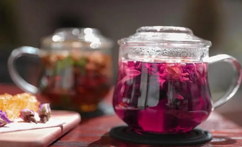 دم نوش گرم و خوشرنگ گل محمدی بنفش و چای میوه‌ای در لیوان‌های شیشه‌ای چیتر چیکن، با عسل طبیعی و غنچه گل.