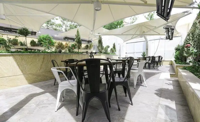 تصویری از فضای دلنشین و سرسبز بیرونی فست فود چیتر چیکن با چیدمان میز و صندلی‌های شیک زیر سایبان‌های مدرن.