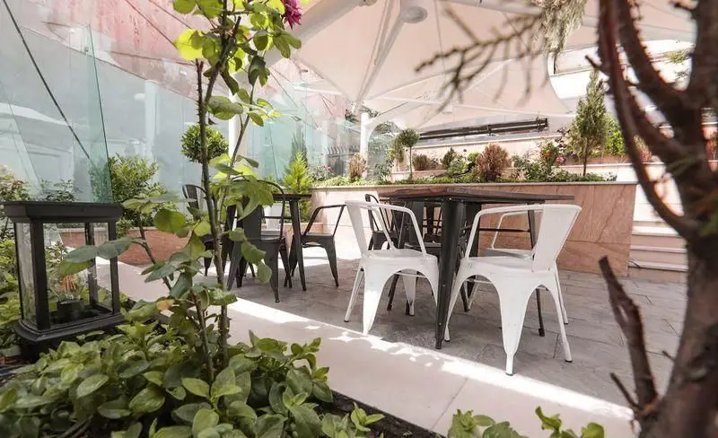 فضای باز دلنشین فست فود چیتر چیکن با میز و صندلی مدرن، سایه‌بان بزرگ و گل و گیاه سرسبز، محیطی ایده‌آل برای صرف غذا.