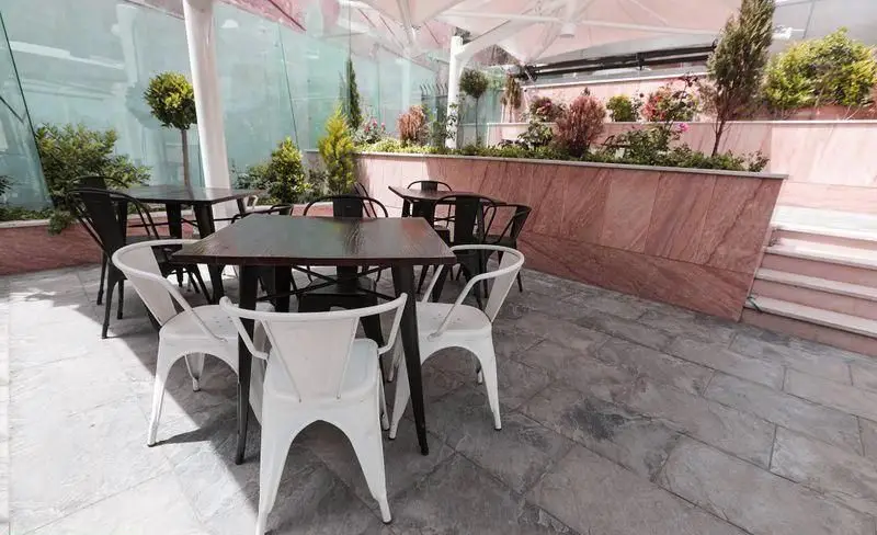 فضای نشیمن روباز فست فود چیتر چیکن با میزهای تیره، صندلی‌های مدرن سفید و مشکی، گیاهان زیبا و سایبان، محیطی دلنشین برای مشتریان.