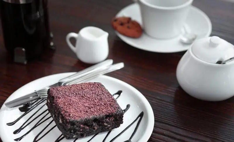 کیک براونی شکلاتی با پودر توت فرنگی، به همراه چنگال و چاقو روی میز چوبی در فست فود چیتر چیکن. سرو شده با قهوه، شکر و شیر برای دسر.