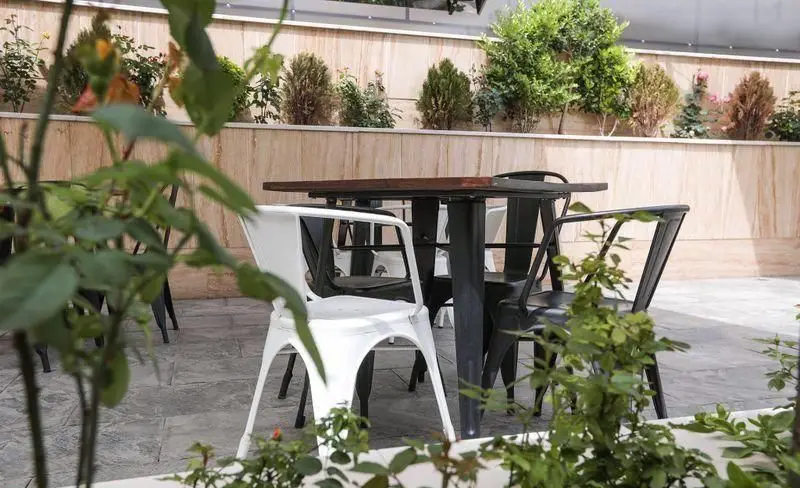 فضای باز سرسبز فست فود چیتر چیکن با میزهای چوبی تیره و صندلی‌های فلزی سفید و مشکی برای تجربه‌ای دلنشین.