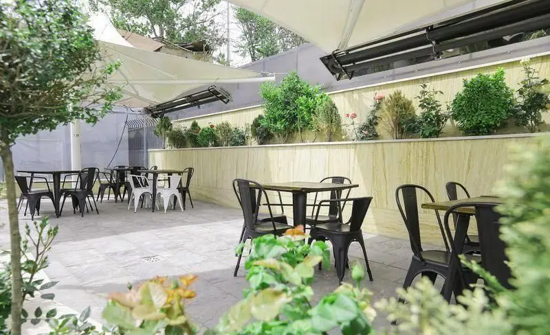 فضای باز رستوران فست فود چیتر چیکن با میز و صندلی‌های مدرن، سایبان‌های شیک و گل و گیاه زیبا برای تجربه‌ای دلنشین در محیطی سرسبز.