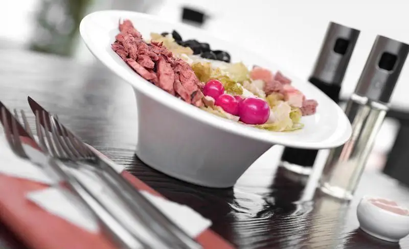 سالاد چیکن لذیذ فست فود چیتر چیکن: فیله مرغ، زیتون، کاهو و گوجه‌فرنگی گیلاسی صورتی در یک کاسه سفید، انتخابی سالم و عالی.