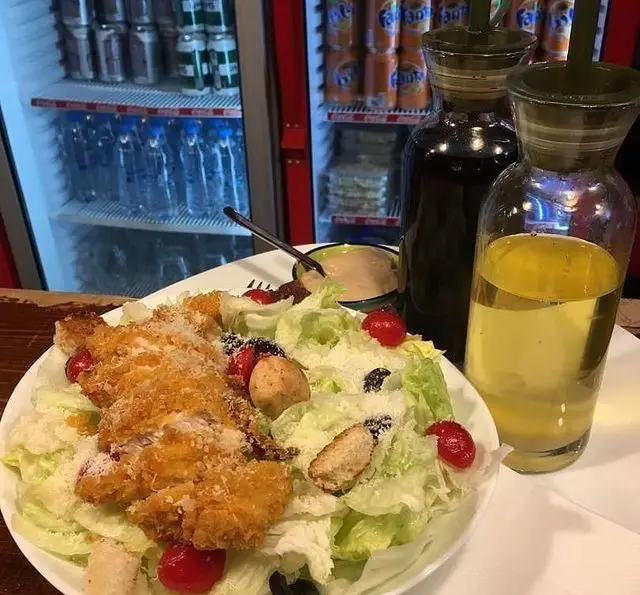 سالاد سزار خوشمزه با مرغ سوخاری در کافه رستوران استیج به همراه روغن زیتون و نوشیدنی‌های موجود در یخچال، آماده سرو.