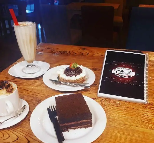 نمایی از میز سرو در کافه رستوران استیج: میلک شیک، تارت توت فرنگی، کیک شکلاتی و قهوه. تجربه‌ای دلپذیر از دسرها و نوشیدنی‌ها در فضایی آرام.