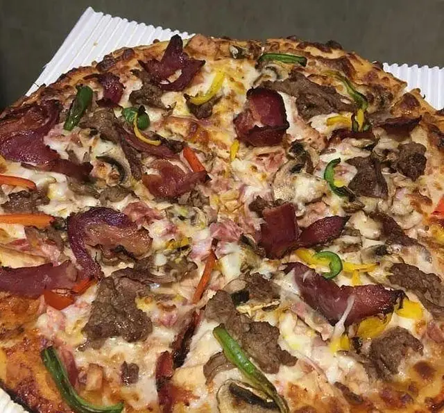 تصویری نزدیک از پیتزای مخصوص کافه رستوران استیج، پر از پنیر، گوشت‌های متنوع، قارچ و فلفل دلمه‌ای رنگی. لذت یک فست فود عالی.