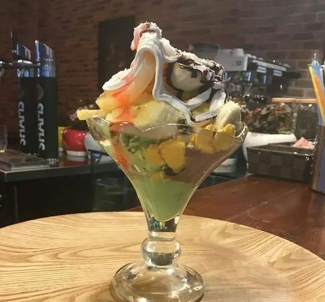 یک پارفه خوش‌رنگ و اشتها‌آور شامل بستنی و میوه در کافه رستوران استیج، تجربه‌ای شیرین در محیطی گرم و دلپذیر.