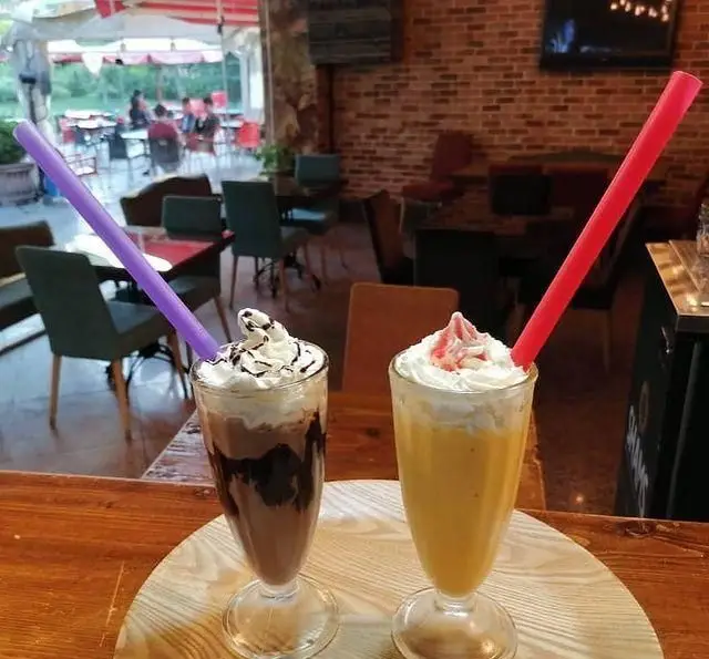 تصویری دلنشین از دو میلک شیک لذیذ با تزئینات خامه در فضای گرم و دنج کافه رستوران استیج برای مشتریان.
