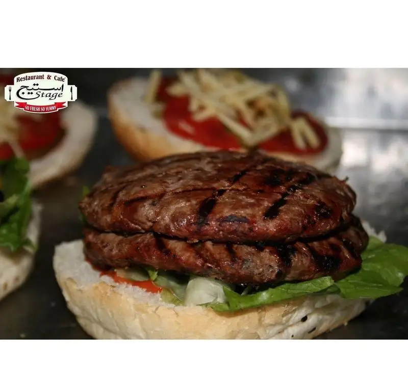 تصویر نزدیک از همبرگر دوبل گریل شده کافه رستوران استیج. گوشت تازه و آبدار، با نان، کاهو و سس، آماده سرو. سوپرایز خوشمزه!