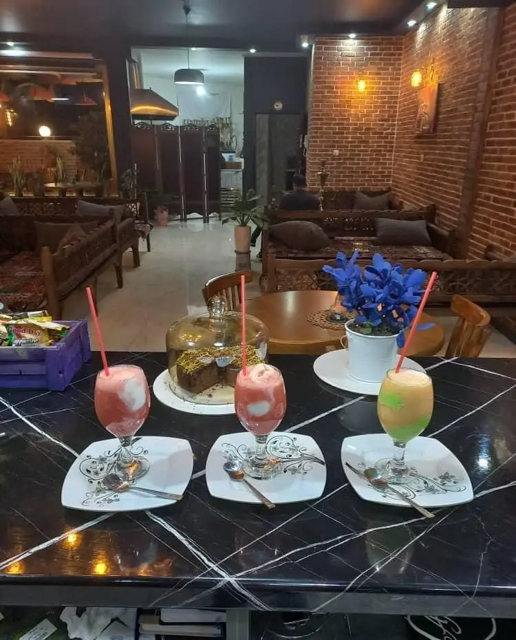 کافه پناه: نمایی از فضای داخلی دنج و سنتی با میزهای چوبی، دیوار آجری، نوشیدنی‌های رنگارنگ و دسر شکلاتی.