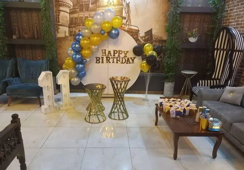 دکور جشن تولد زیبا و خاص در کافه پناه، با بادکنک آرایی آبی و طلایی، اعداد نوری 11 و میز شیرینی و دسر. فضایی شیک برای میزبانی تولد.