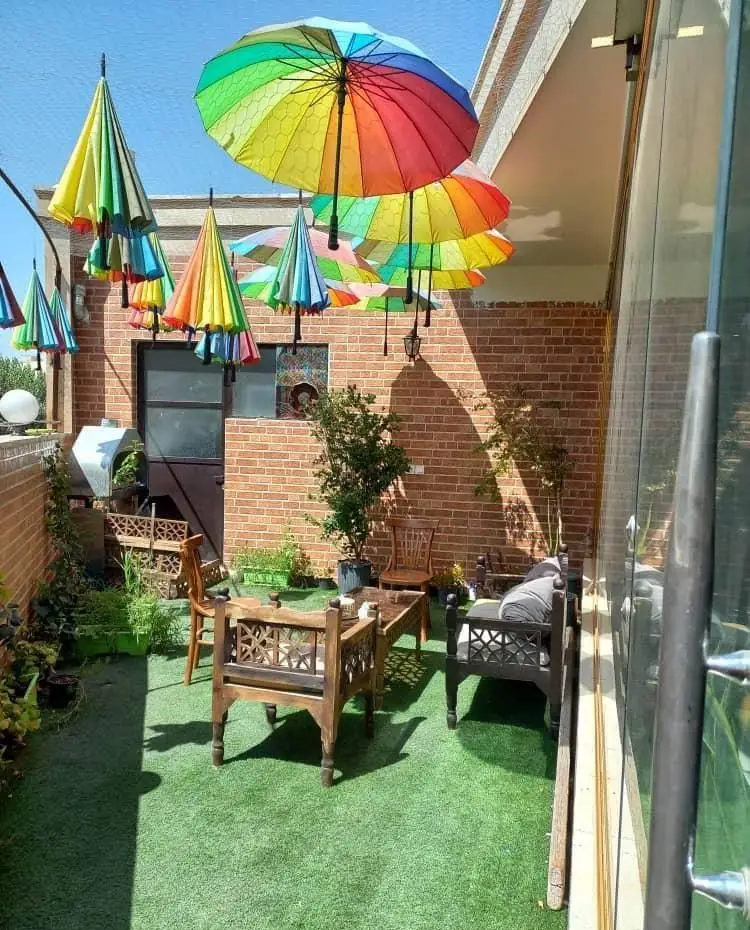 کافه پناه: تراس روباز زیبا با چترهای رنگارنگ شاد، مبلمان چوبی دست‌ساز و فضای سبز چمن. محیطی ایده‌آل برای آرامش و دورهمی.