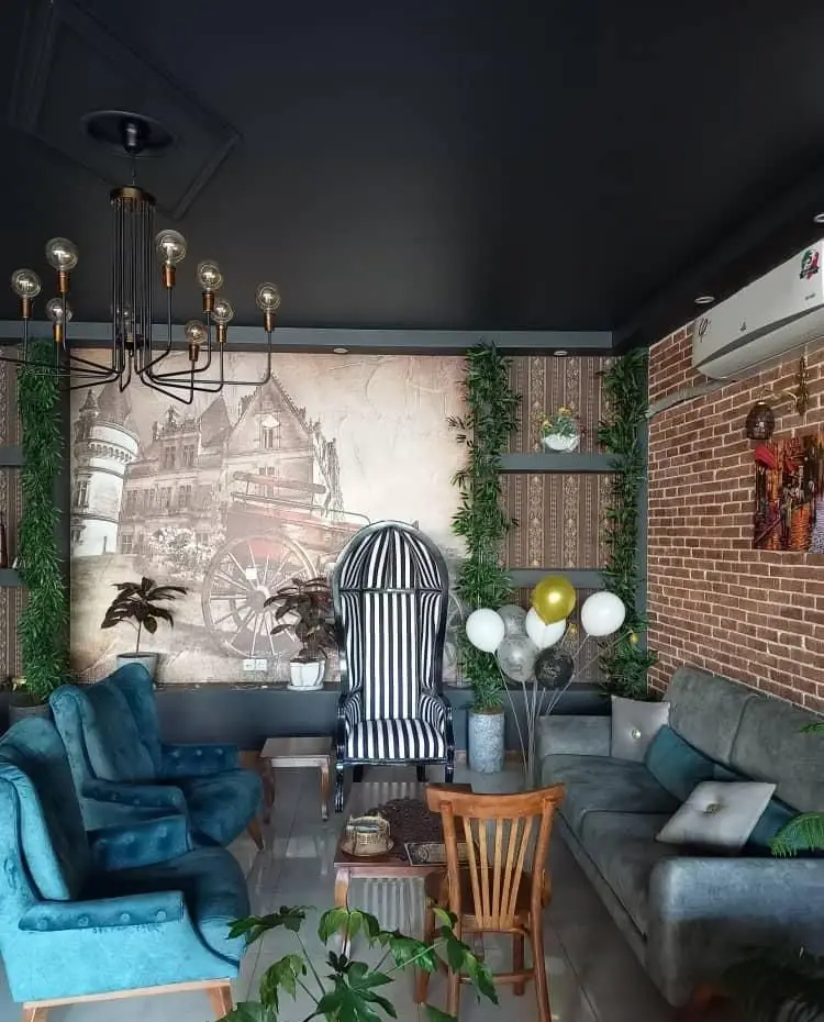 فضای داخلی کافه پناه با دکوراسیون شیک و کلاسیک، شامل مبلمان مخملی آبی، صندلی طرح‌دار، لوستر و دیوار آجری، محیطی دنج و جذاب