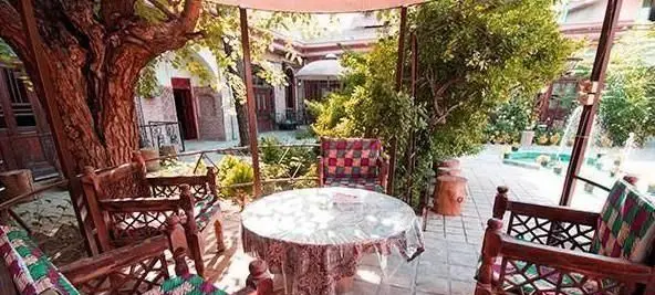 فضای سنتی و دلنشین رستوران باغ شازده با حیاط سرسبز، درخت کهنسال، حوض و فواره، و میز و صندلی چوبی در محیطی آرام.