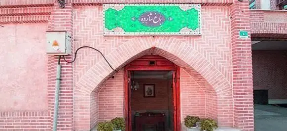 نمای بیرونی و ورودی اصلی رستوران سنتی باغ شازده با معماری آجری زیبا، درب چوبی قرمز و تابلوی سبز رنگ چشم‌نواز