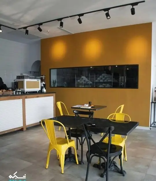 نمای داخلی شیک و مدرن کافه نانوایی پاتیس: میز و صندلی‌های جذاب زرد و مشکی، پیشخوان دستگاه قهوه و ویترین کامل نان و شیرینی تازه.