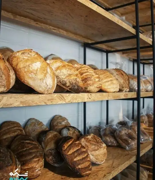 انواع نان‌های تازه و خوش‌عطر کافه نانوایی پاتیس روی قفسه‌های چوبی، شامل نان‌های سنتی و بسته‌بندی شده برای فروش روزانه.