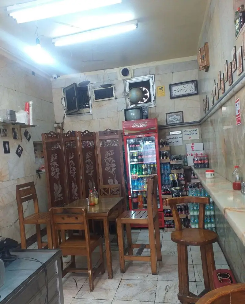 فضای داخلی ساندویچ آذر، فست فود دنج با میز و صندلی چوبی، یخچال نوشیدنی و پیشخوان آماده سرو سفارشات.