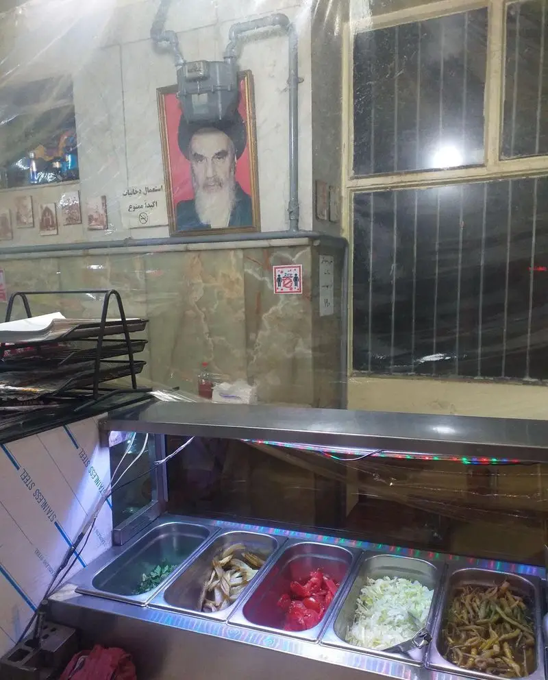 نمای داخلی ساندویچ آذر با پیشخوان استیل و سینی‌های حاوی مواد اولیه تازه شامل سبزیجات، گوجه و کلم برای ساندویچ‌های خوشمزه.