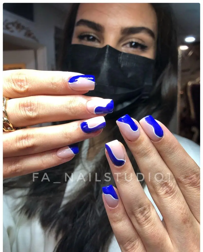 طراحی ناخن شیک و مدرن با لاک ژل آبی کاربنی و کرم به صورت فرنچ موجدار دخترانه در سالن تخصصی کاشت و دیزاین ناخن
