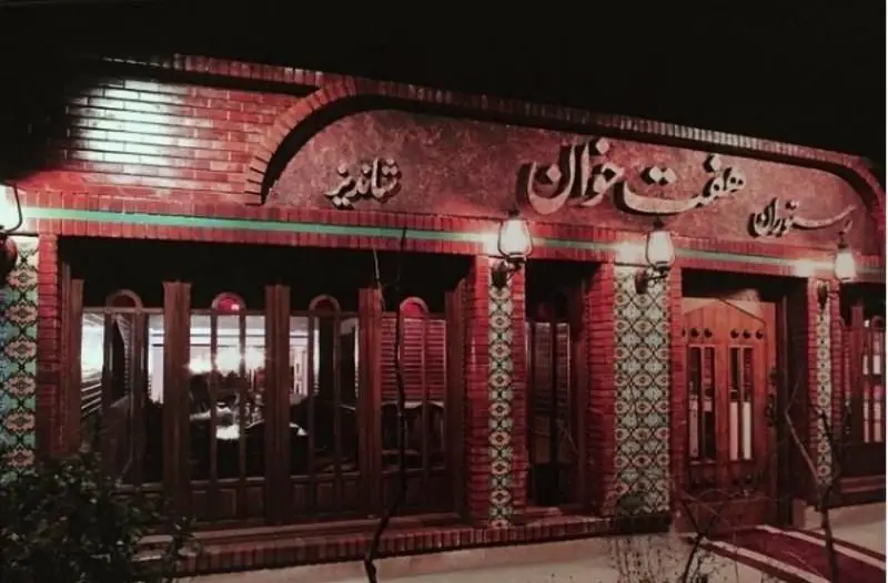 تصویر نمای بیرونی شبانه رستوران هفت خوان شیراز، با طراحی سنتی آجری و کاشی‌کاری، ورودی‌های چوبی و تابلو نانوایی روشن.