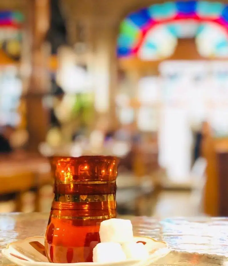 استکان چای آذری با قند در سفره خانه سنتی، لذت نوشیدنی گرم در فضایی دلنشین با دکوراسیون رنگارنگ و اصیل.