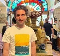 مردی خوشرو در فضای گرم و دلنشین سفره خانه سنتی آذری، در پس‌زمینه ساماوار طلایی بزرگ و سقف شیشه‌های رنگی سنتی دیده می‌شود.