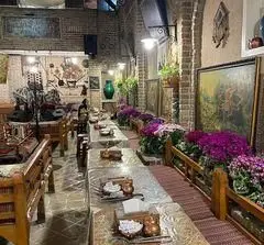 فضای داخلی سفره خانه سنتی آذری با دکوراسیون گرم و سنتی ایرانی، میزهای چوبی بلند و گلدان‌های گل زیبا. مناسب برای تجربه غذای اصیل ایرانی.